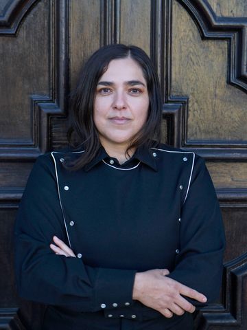 Josette Melchor against a dark carved wood door, in color.