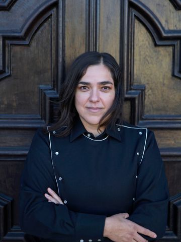 Josette Melchor, arms crossed, wide crop against a wood door.