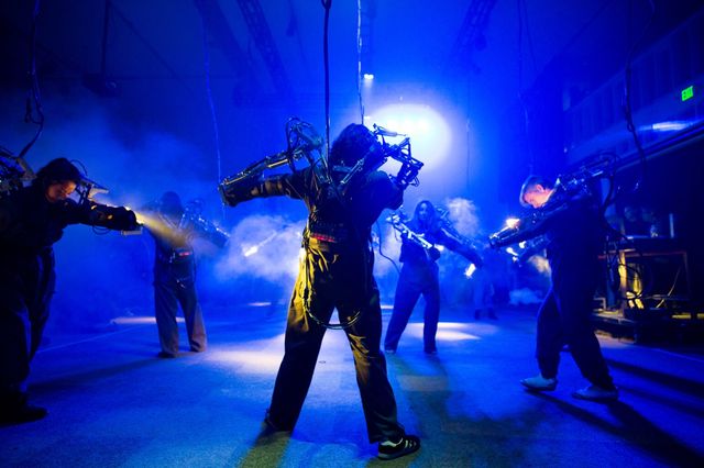 Performers in light-reactive robotic exosuits during the US premiere of Inferno, bathed in deep blue stage light.
