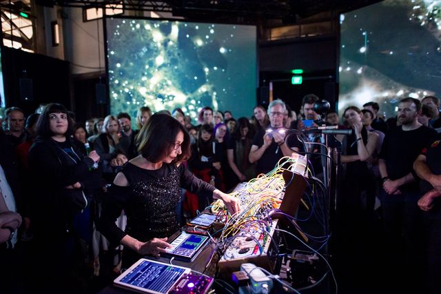 Suzanne Ciani performing live on a modular synthesizer to a crowd, projections behind her.